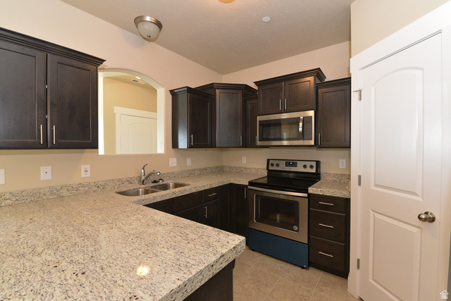 241 West Ridge Road Saratoga Springs, UT 84045 - Photo 6 of 21 Kitchen featuring dark wood cabinetry, light speckled countertops, stainless steel appliances, and tile flooring