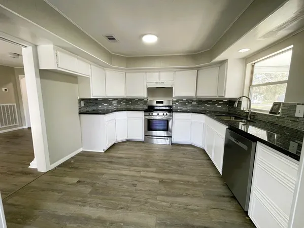 a kitchen with stainless steel appliances granite countertop a stove top oven a sink a refrigerator white cabinets and wooden floor