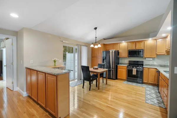 a kitchen with stainless steel appliances kitchen island granite countertop a refrigerator a stove top oven and a dining table with wooden floor