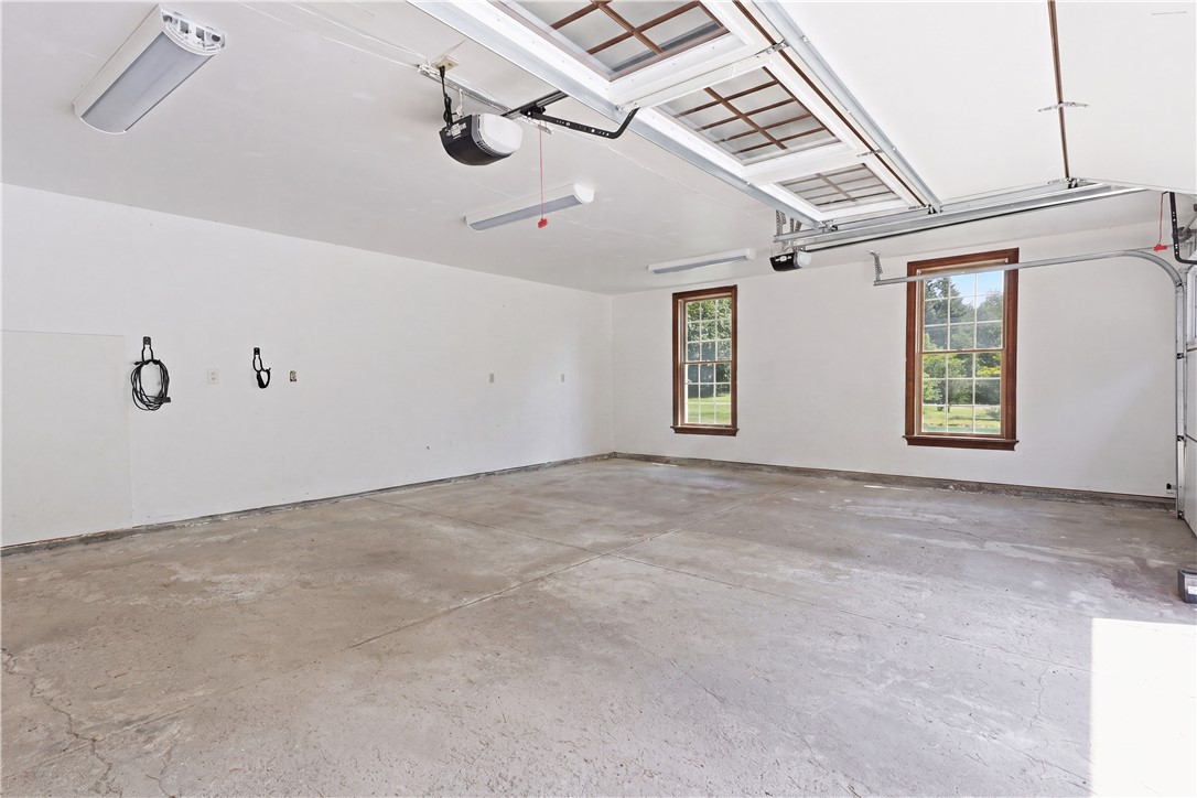 2057 Stirnie Road Victor, NY 14564 - Photo 39 of 48 The property features an expansive attached garage space, complete with a solid poured concrete floor, bright overhead lighting fixtures, and large dual windows that offer plenty of natural light. Equipped with an automatic garage door opener, this deep layout provides extensive room for vehicle parking, secondary storage, or a dedicated home workshop space.