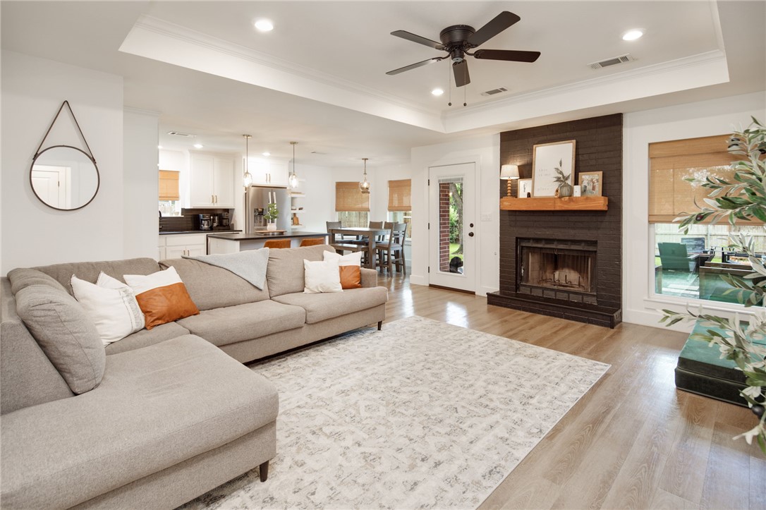 4700 Kensington Road Bryan, TX 77802 - Photo 6 of 31 Spacious living area featuring light wood-finish flooring, a dark brick fireplace with a wood mantel, tray ceilings, and built-in floating shelf