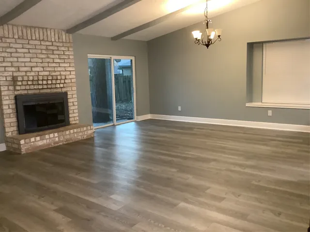 an empty room with wooden floor fireplace and windows