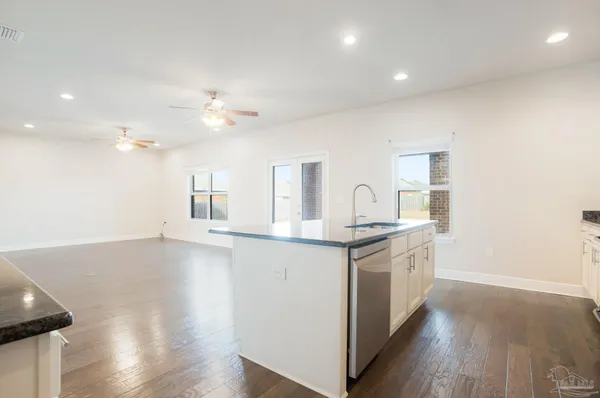 a view of an empty room and kitchen with wooden floor