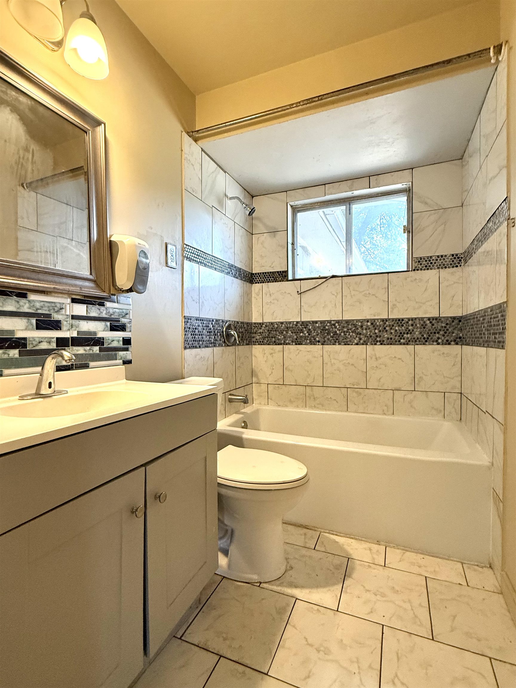 2930 Getwell Road Memphis, TN 38118 - Photo 15 of 25 Bathroom featuring a tiled tub/shower combination with mosaic accents, a built-in window, and a vanity with an integrated sink and base cabinetry