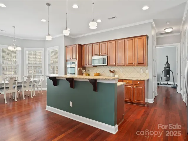 a kitchen with granite countertop a stove top oven a sink a dining table and chairs with wooden floor