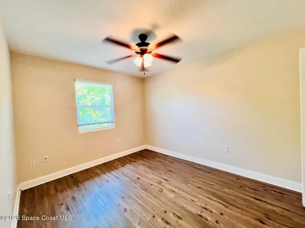 an empty room with wooden floor fan and windows