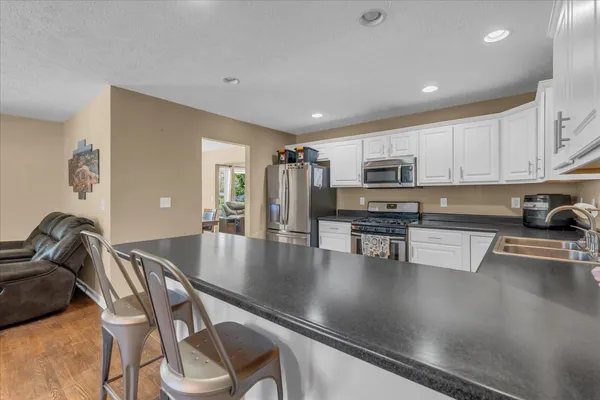 a kitchen with stainless steel appliances granite countertop a stove top oven a sink a dining table and chairs with wooden floor
