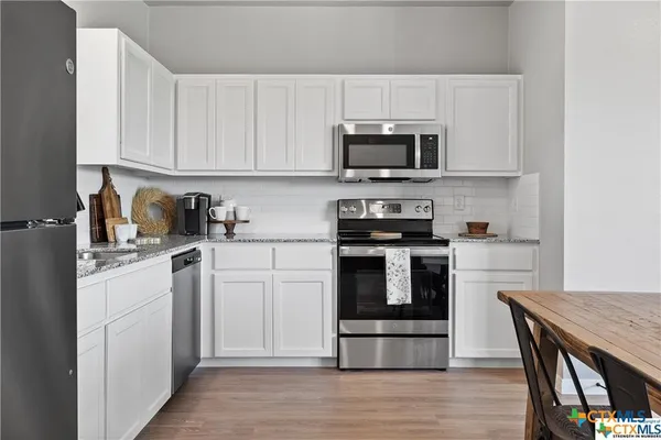 a kitchen with stainless steel appliances granite countertop a stove top oven a sink dishwasher and white cabinets with wooden floor