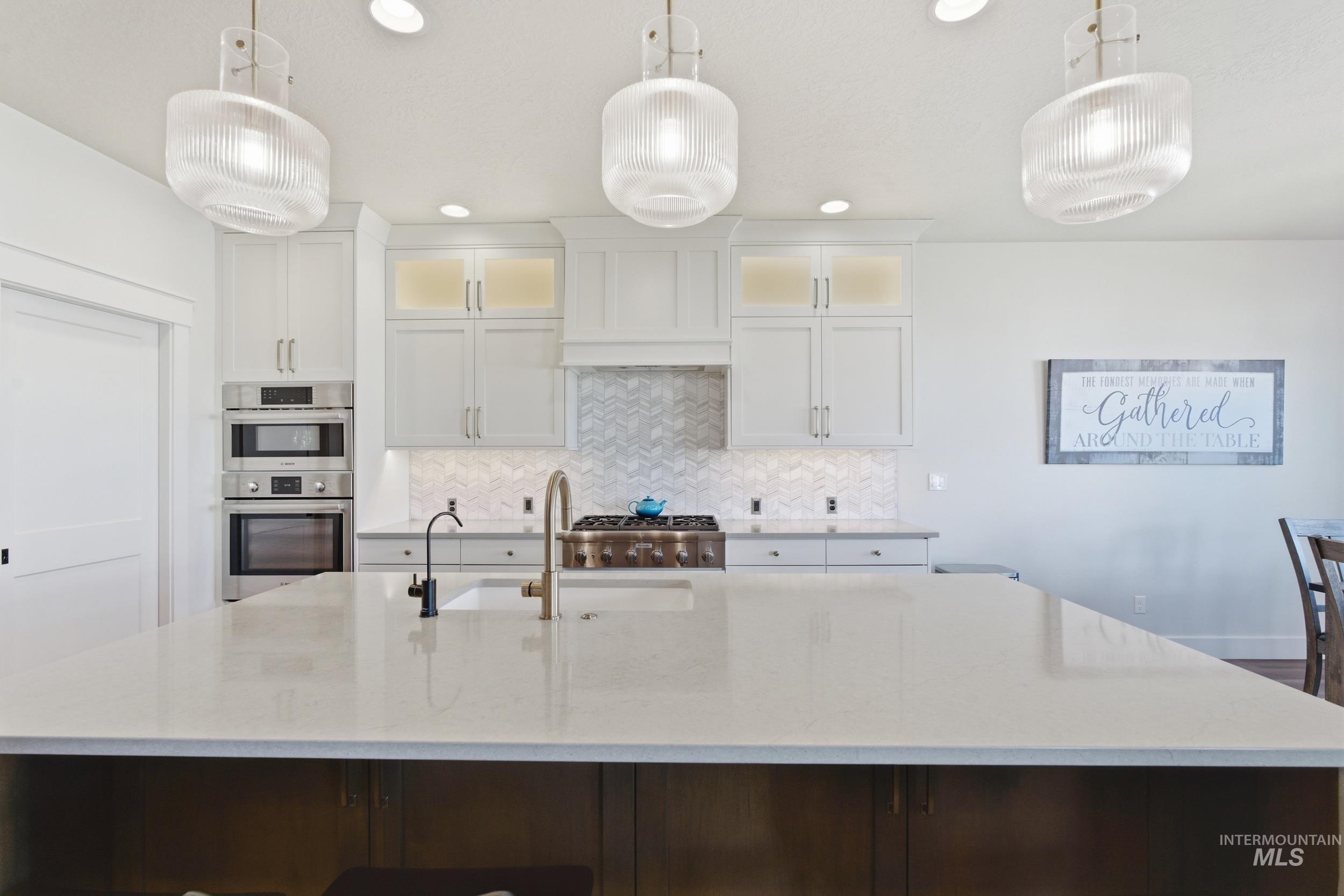 6347 South Utmost Lane Meridian, ID 83642 - Photo 9 of 37 Kitchen featuring a large central island with a light-colored countertop, white cabinetry with upper glass-front accents, stainless steel double ovens, a gas range, and a herringbone pattern tile backsplash