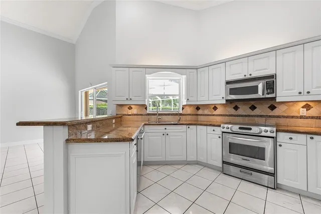 a kitchen with granite countertop white cabinets appliances a sink and a window