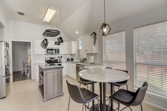 a kitchen with stainless steel appliances granite countertop a dining table chairs stove and white cabinets