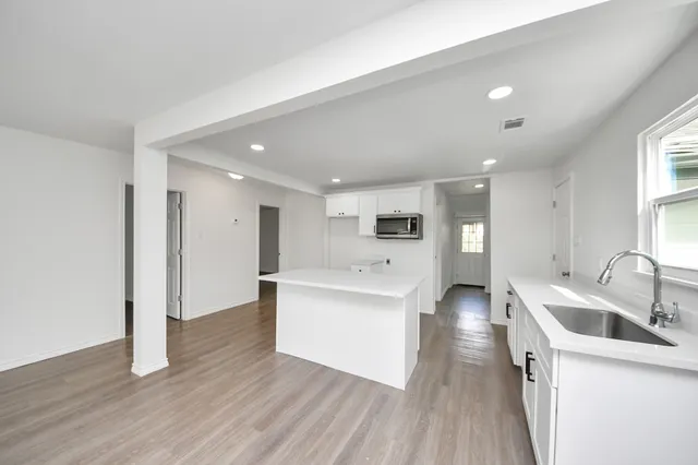 a view of a kitchen with kitchen island a sink wooden floor and a living room