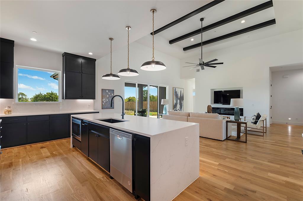 430 Whispering Way Red Oak, TX 75154 - Photo 17 of 40 Open-concept living space featuring wood-finish flooring, a kitchen island with integrated sink, black cabinetry, stainless steel dishwasher, and a living area with a vaulted ceiling and exposed beams
