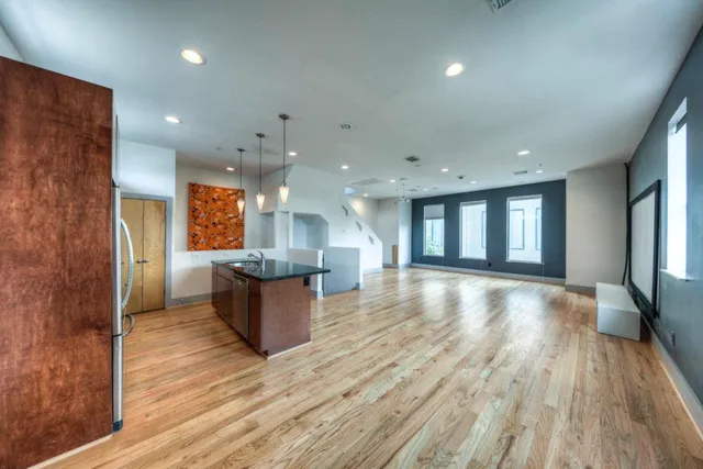 a view of an empty room and kitchen with a wooden floor
