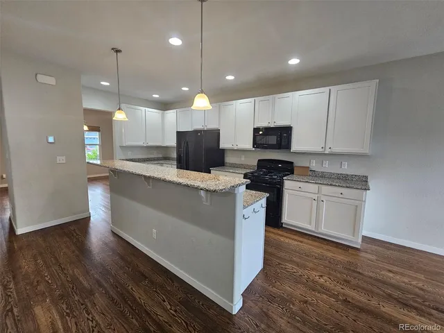 a kitchen with kitchen island granite countertop stainless steel appliances a stove a sink a microwave a refrigerator and white cabinets with wooden floor