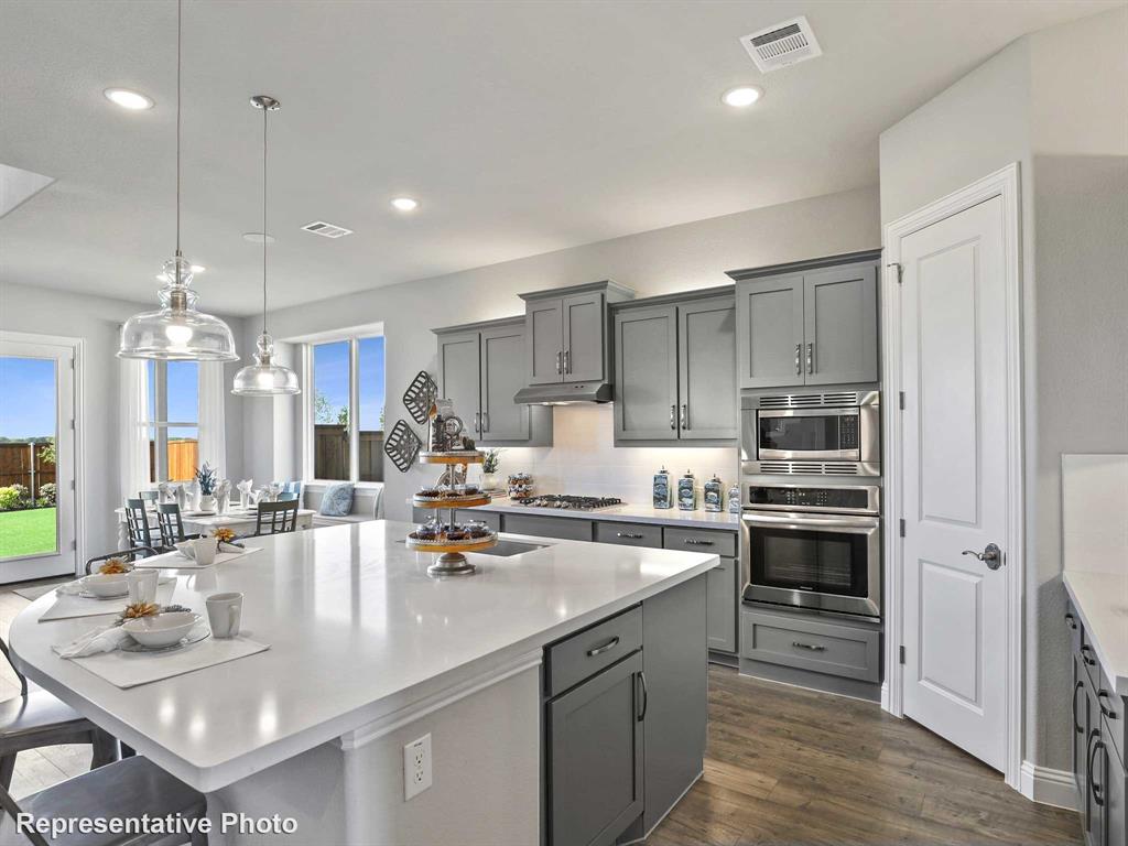 1143 Rothland Lane Red Oak, TX 75154 - Photo 4 of 18 Contemporary kitchen featuring a large central island with a solid surface countertop, grey cabinetry, stainless steel appliances, and wood-finish flooring