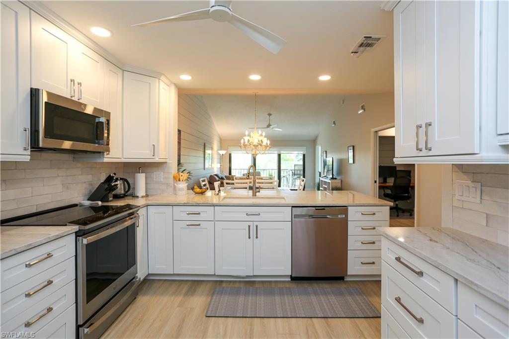 5733 Deauville Circle, Unit G308 Naples, FL 34112 - Photo 9 of 50 a kitchen with stainless steel appliances granite countertop a stove top oven a sink dishwasher and a refrigerator with wooden cabinets