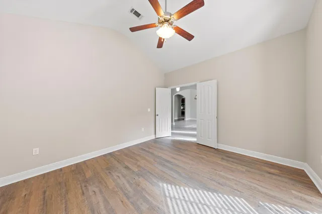 an empty room with wooden floor ceiling fan and windows