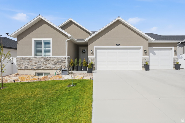 712 West 660 South Tooele, UT 84074 - Photo 1 of 1 View of front of property featuring stone siding, an attached garage, stucco siding, a front yard, and concrete driveway