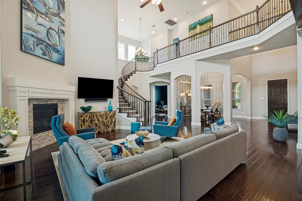 388 Bethany Road Sunnyvale, TX 75182 - Photo 8 of 40 Two-story living area featuring dark pre engineered wood-finish flooring, a stone-faced fireplace with a white mantel, and a grand curved staircase with wrought iron balusters