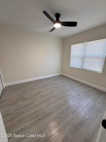 an empty room with wooden floor fan and windows