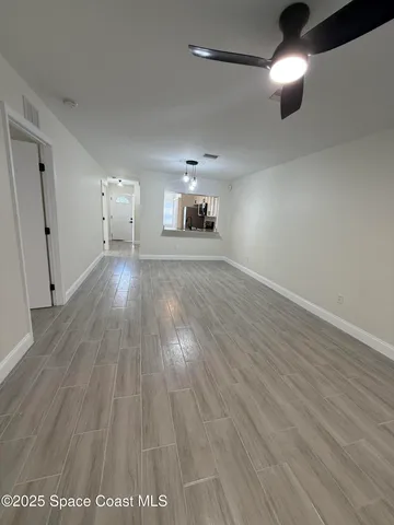 an empty room with wooden floor ceiling fan and windows