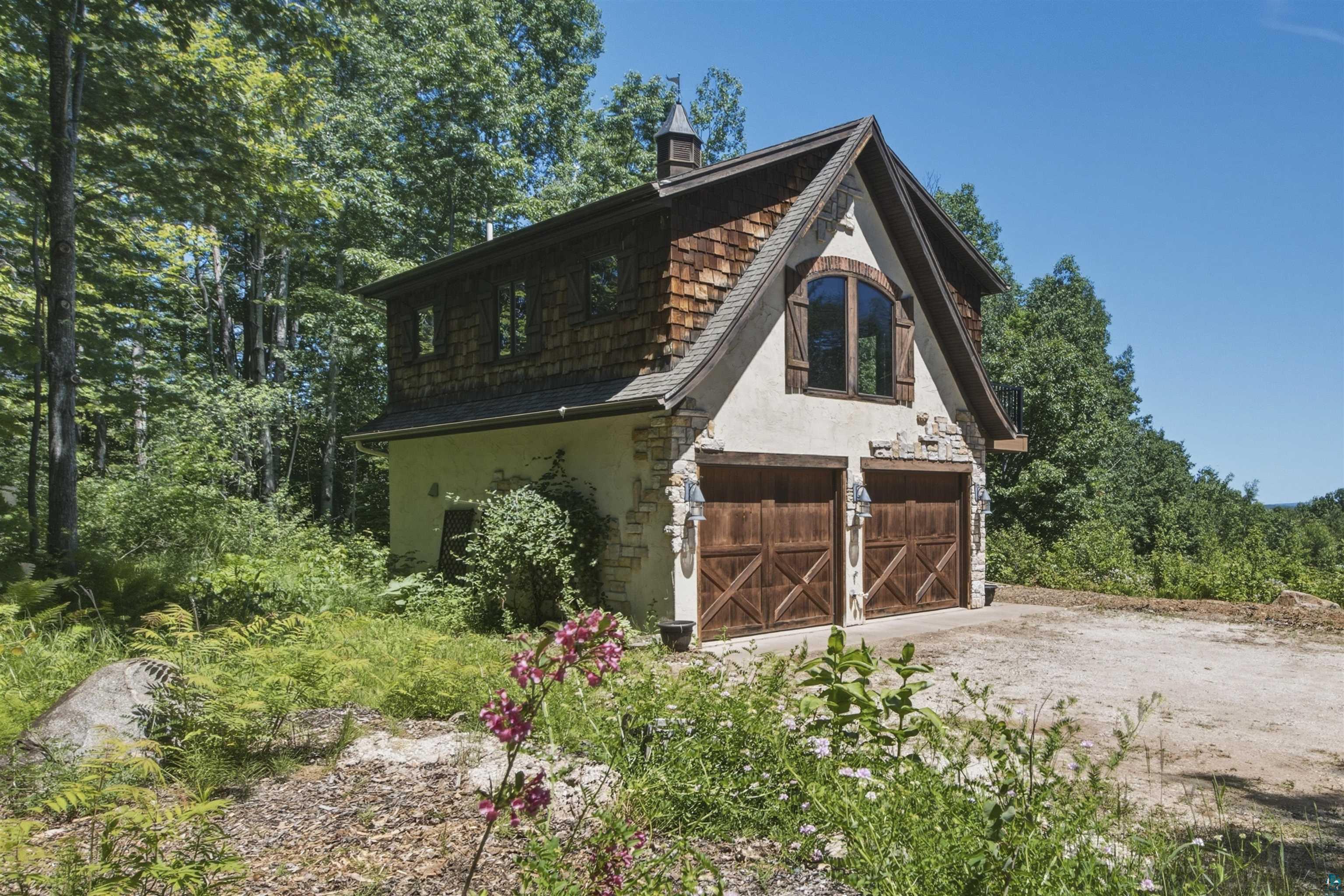 Two-story structure featuring a stucco and stone veneer base, wood-finish garage doors with decorative hardware, and a shingle roof with a prominent arched window on the upper level