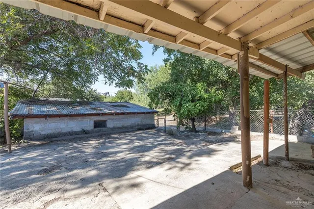 a backyard of a house with large trees and a wooden bench
