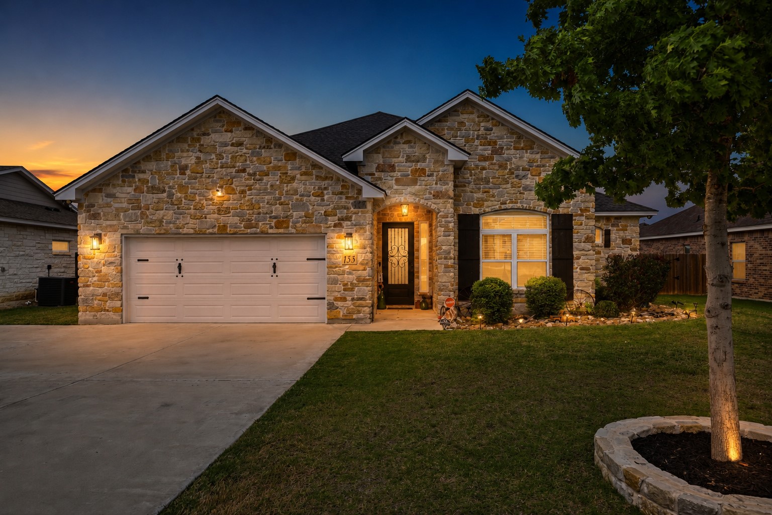 133 Greg Lane Jarrell, TX 76537 - Photo 1 of 24 Stone facade residence featuring a two-car garage, covered entry, front landscaping, and exterior lighting