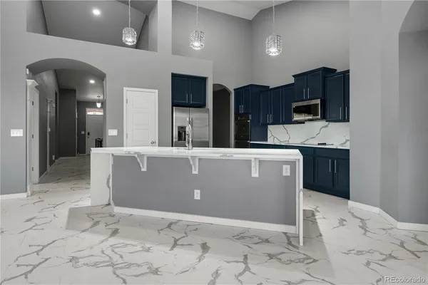 a room with stainless steel appliances kitchen island granite countertop a refrigerator and a sink