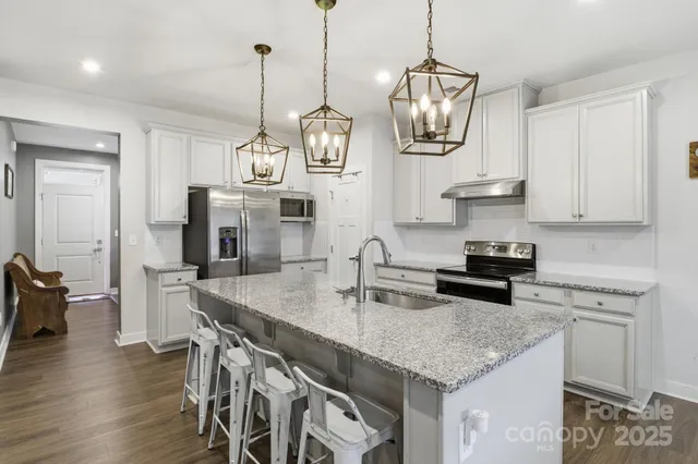 a kitchen with stainless steel appliances granite countertop a sink a stove and a wooden floor