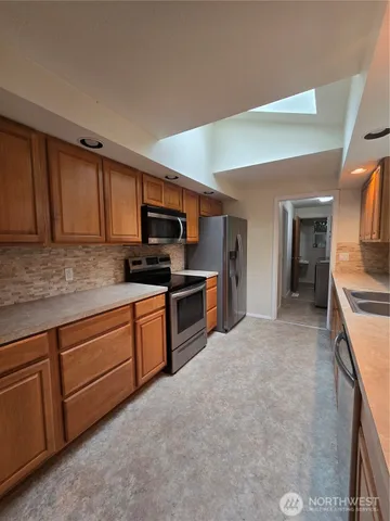 a kitchen with stainless steel appliances granite countertop a stove top oven a sink dishwasher and a refrigerator with wooden cabinets