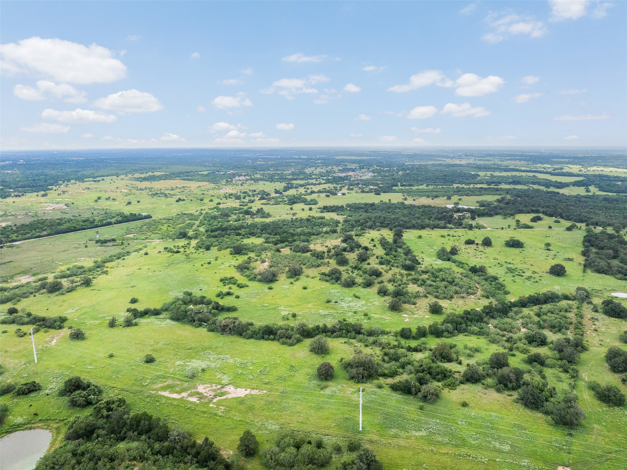Tbd Lot 10 Tbd Road Luling, TX 78648 - Photo 6 of 10 Vast green landscape with scattered trees extends under an open sky, offering abundant natural beauty.