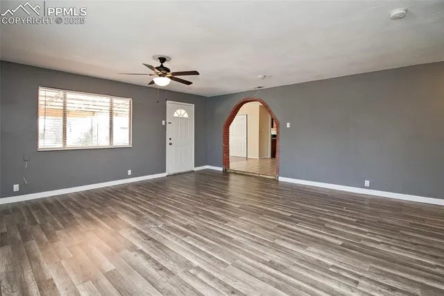 an empty room with wooden floor chandelier fan and windows