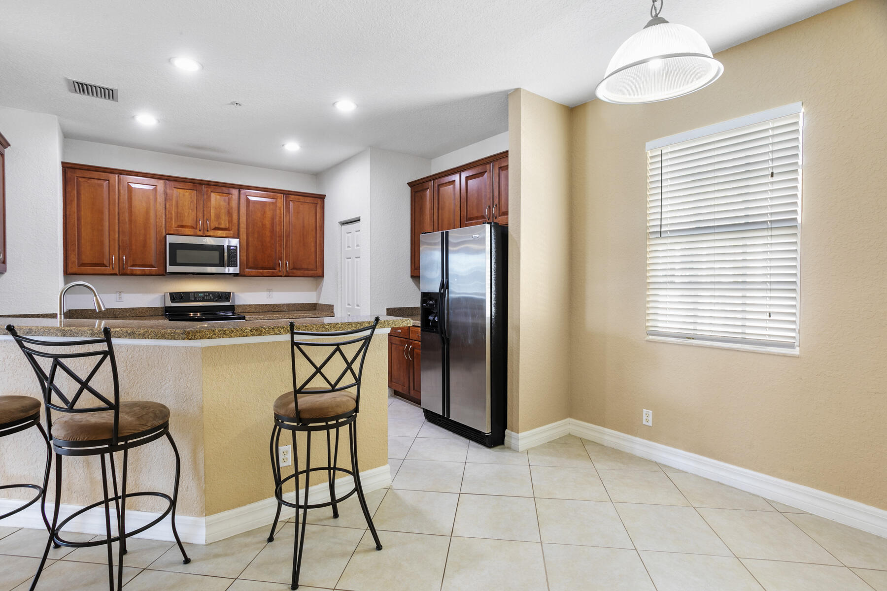 114 Locustberry Lane, Unit 101 Jupiter, FL 33458 - Photo 5 of 59 a kitchen with stainless steel appliances granite countertop a stove a refrigerator a microwave oven with a dining table and chairs