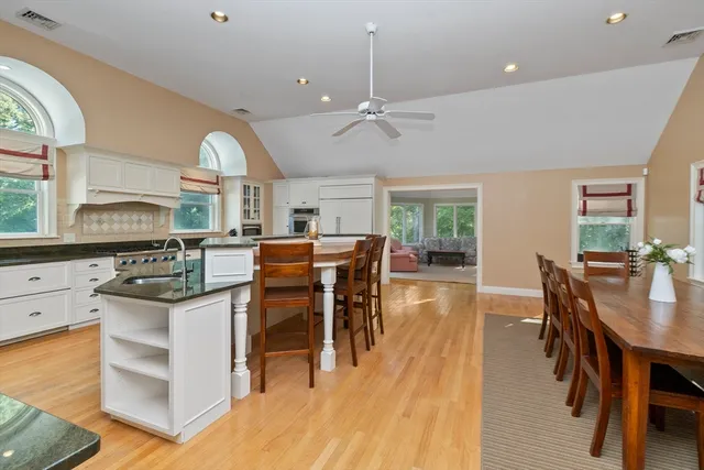 a kitchen with stainless steel appliances kitchen island granite countertop a stove a refrigerator a dining table and chairs with wooden floor