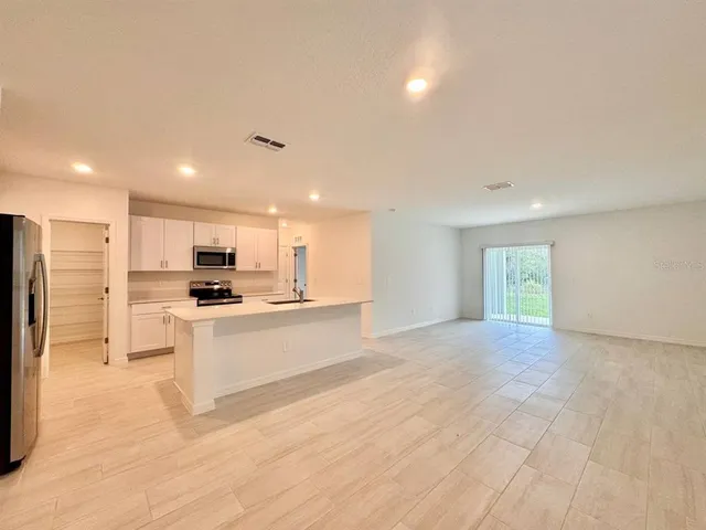 a view of kitchen with stainless steel appliances kitchen island granite countertop a refrigerator a stove a sink dishwasher and white cabinets with wooden floor
