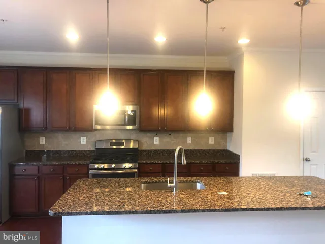 a kitchen with kitchen island granite countertop a sink a stove and a wooden cabinets