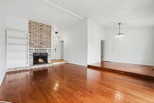 a view of an empty room with wooden floor fireplace and a window