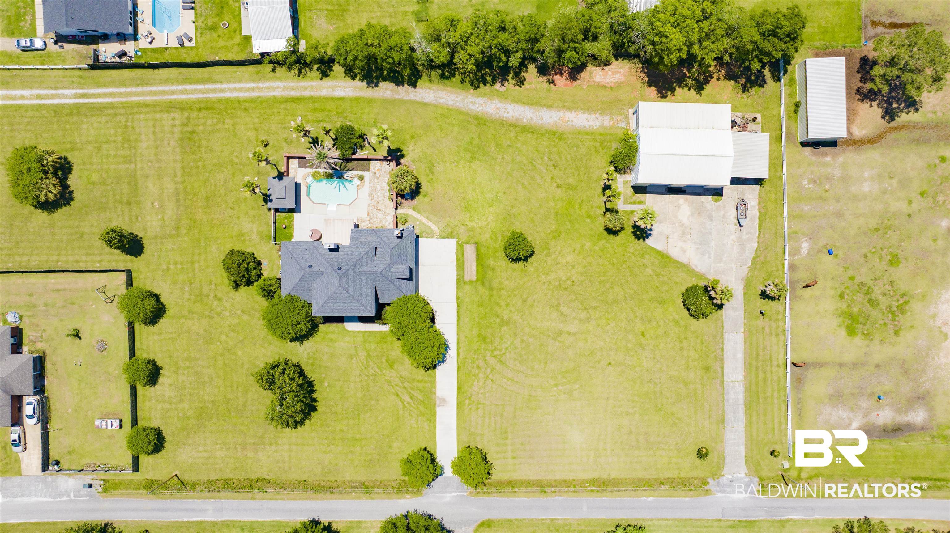 12944 Anna's Way Stapleton, AL 36578 - Photo 10 of 64 Expansive lot featuring a primary residence with a dark shingle roof, a separate large outbuilding, a detached garage, a concrete driveway, and a private swimming pool with stone surround