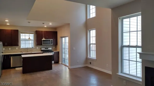 a kitchen with stainless steel appliances granite countertop a refrigerator a sink dishwasher a stove and a dining table with wooden floor