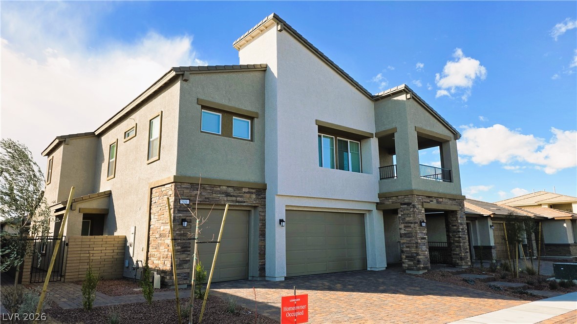 Contemporary house with stone siding, a balcony, stucco siding, a garage, and a gate
