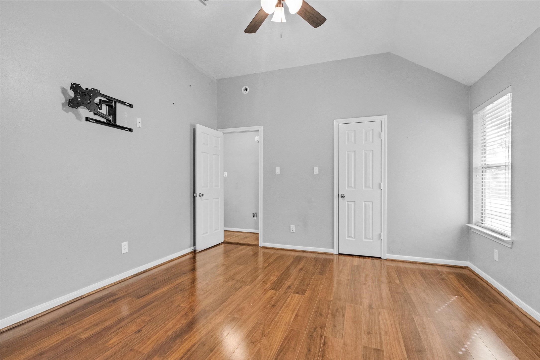 23 Alba Road Montgomery, TX 77356 - Photo 25 of 37 This room features a vaulted ceiling, hardwood floors, and neutral gray walls. It includes a ceiling fan, two doors, and a window that brings in natural light. A wall mount for a TV is already installed, offering convenience for entertainment setup.