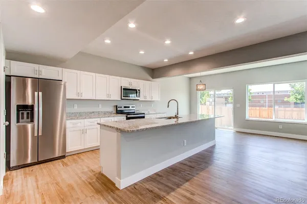 a large kitchen with stainless steel appliances granite countertop a stove a sink dishwasher a refrigerator and white cabinets with wooden floor