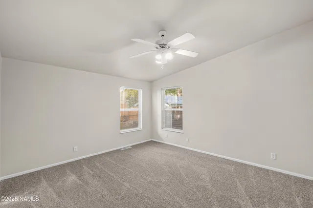 an empty room with chandelier fan and windows
