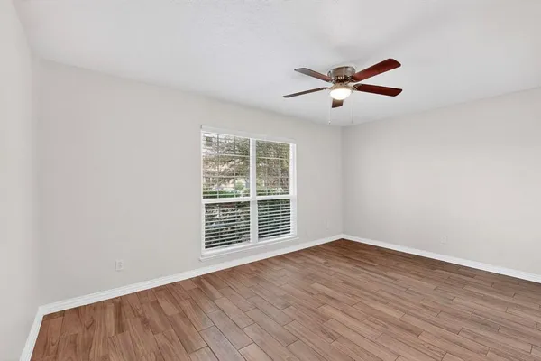 an empty room with wooden floor a ceiling fan and windows