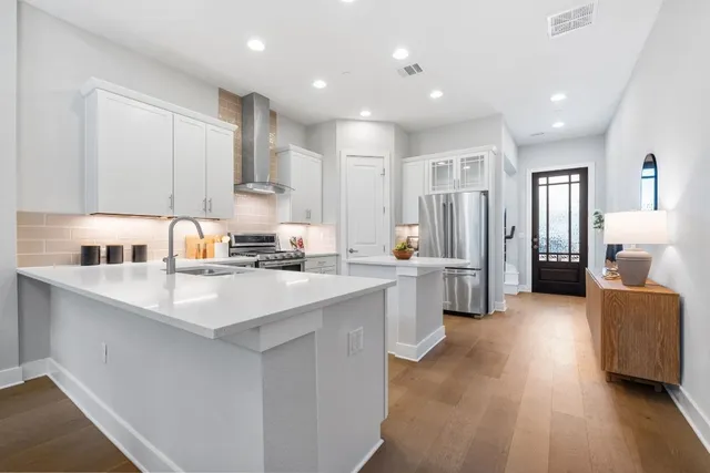 a kitchen with stainless steel appliances granite countertop a refrigerator a sink dishwasher a stove and white cabinets with wooden floor