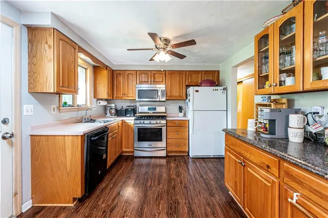 a kitchen with granite countertop a refrigerator a sink dishwasher a stove and white countertops with wooden floor