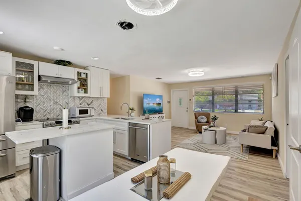 a open kitchen with stainless steel appliances kitchen island granite countertop a sink dishwasher stove and white cabinets with wooden floor