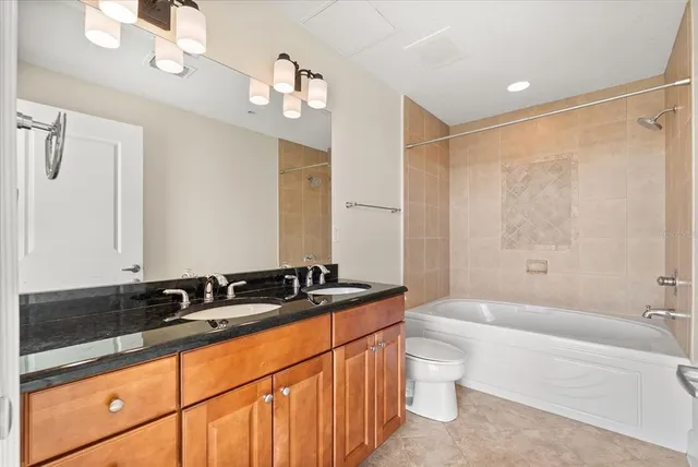 a bathroom with a granite countertop sink a toilet a mirror a bathtub and shower